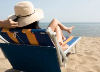 Mujer con pamela sentada en una silla de playa tomando el sol mientras mira al océano