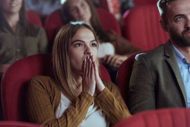 Mujer joven rubia y con chaqueta de cuero marrón asistiendo al teatro y sorprendida por lo que ha visto
